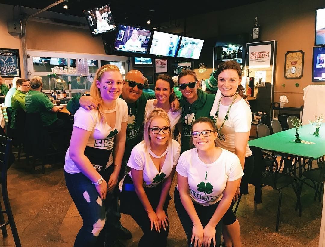 Six people posing together in a dimly lit bar with TVs and a green pool table in the background