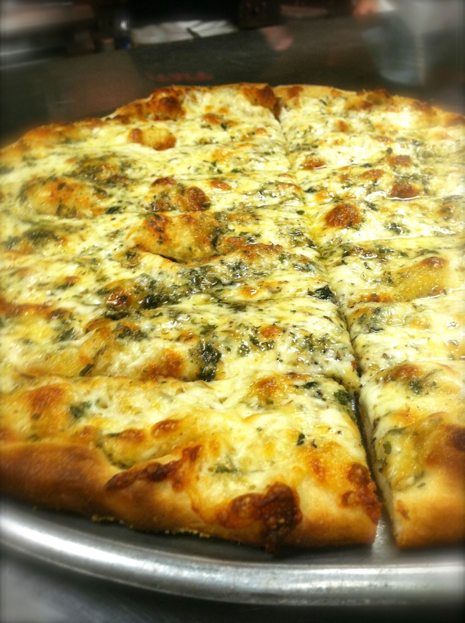 Cheesy baked pizza on a metal tray, cut into slices, with browned crust and herbs