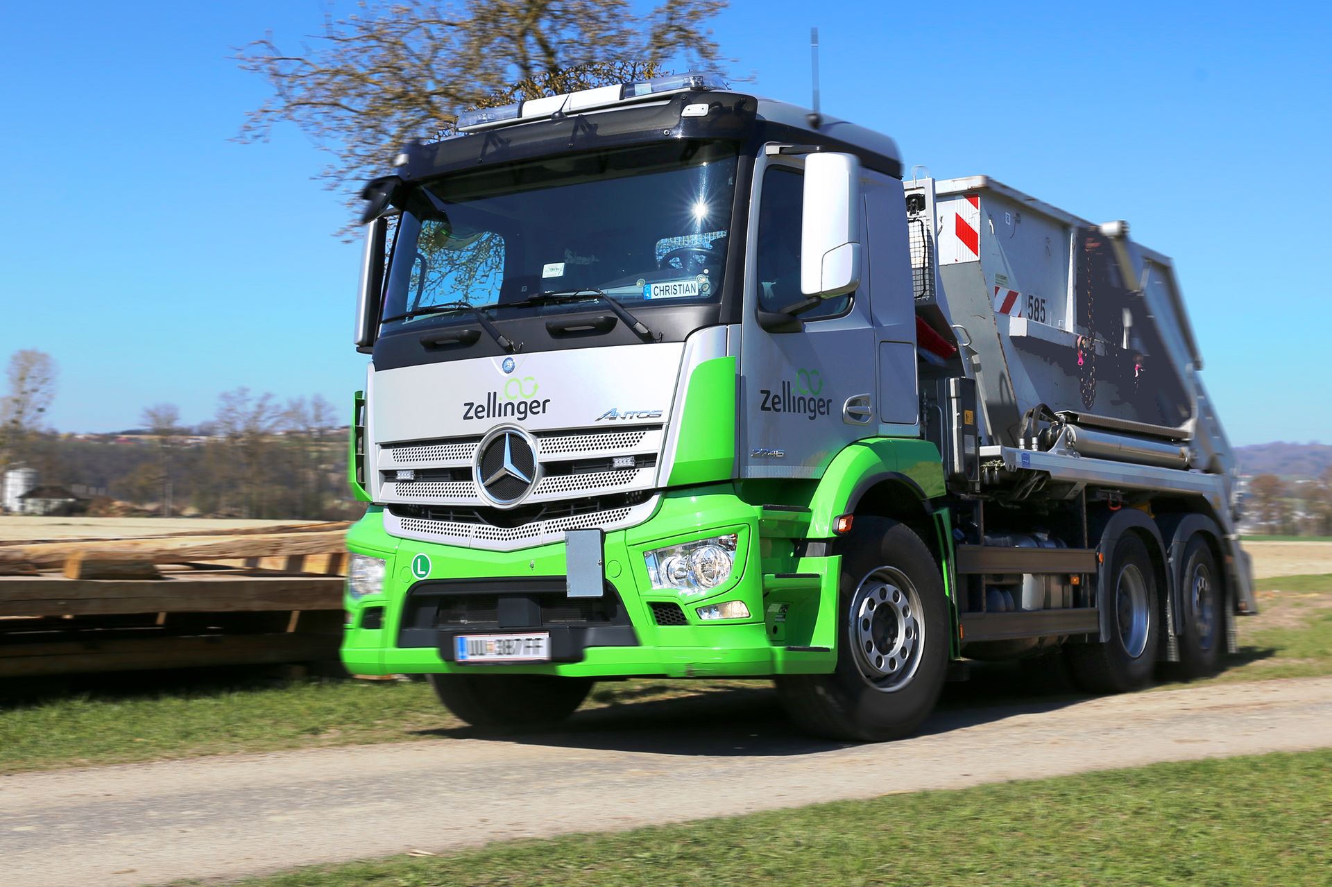 Mercedes truck with silver and green paint on a grassy field under a blue sky.