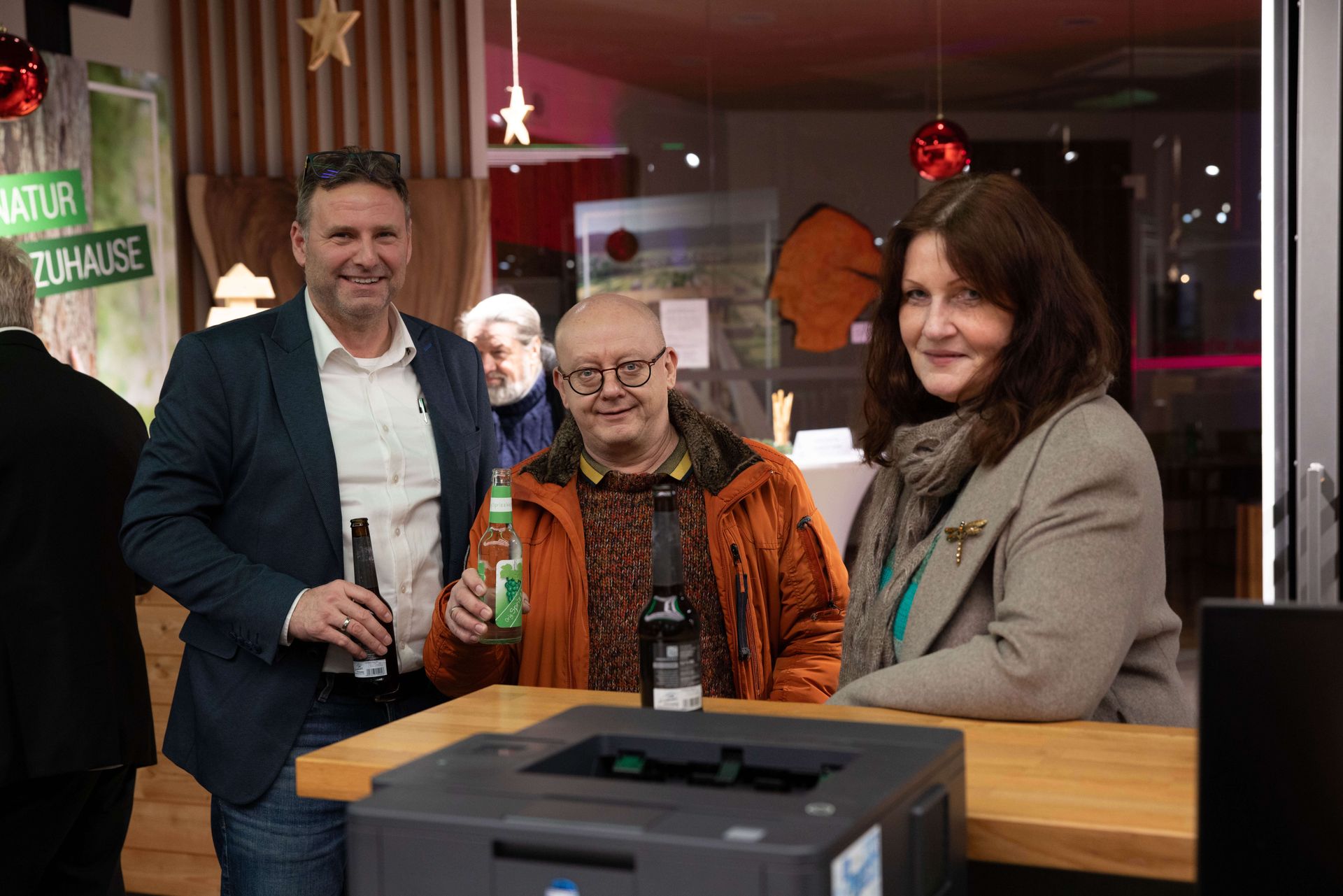 Drei Personen stehen an der Theke und halten lächelnd Getränke in den Händen.