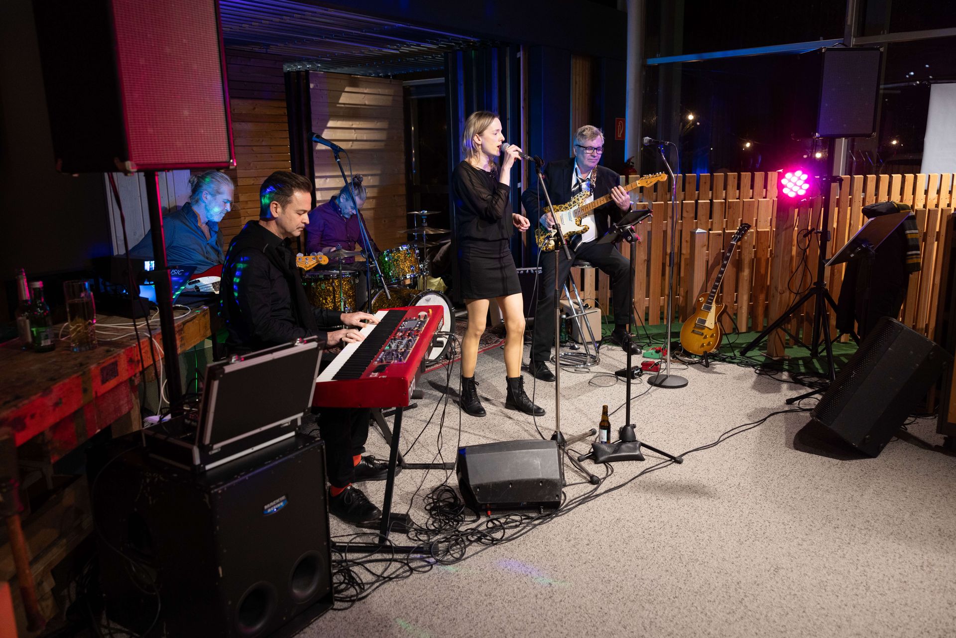 Band performt auf einer Bühne: eine Frau singt, Keyboardspieler, Gitarrist, Schlagzeuger.