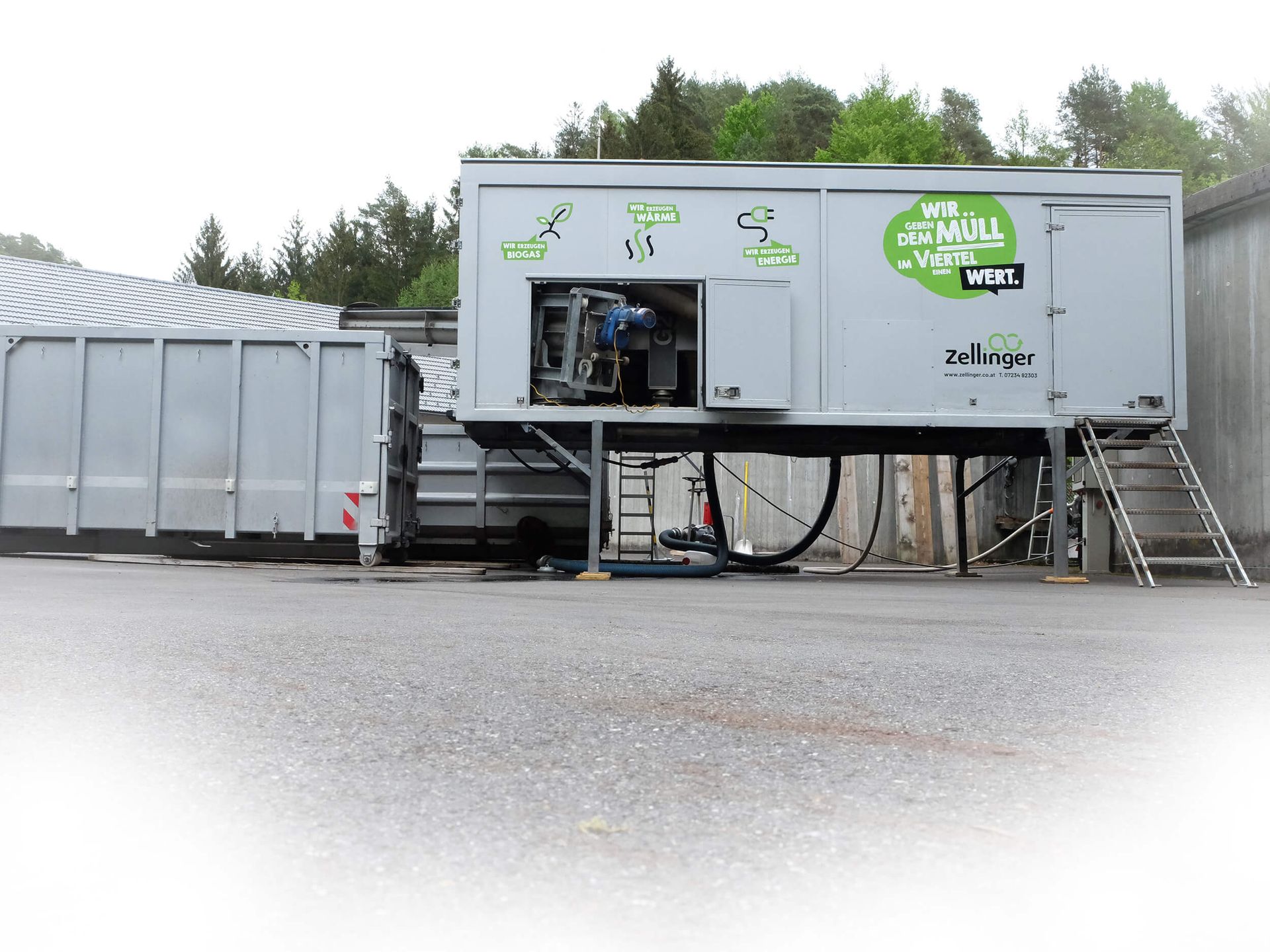 Gray industrial machine with container, outdoors; recycling facility.