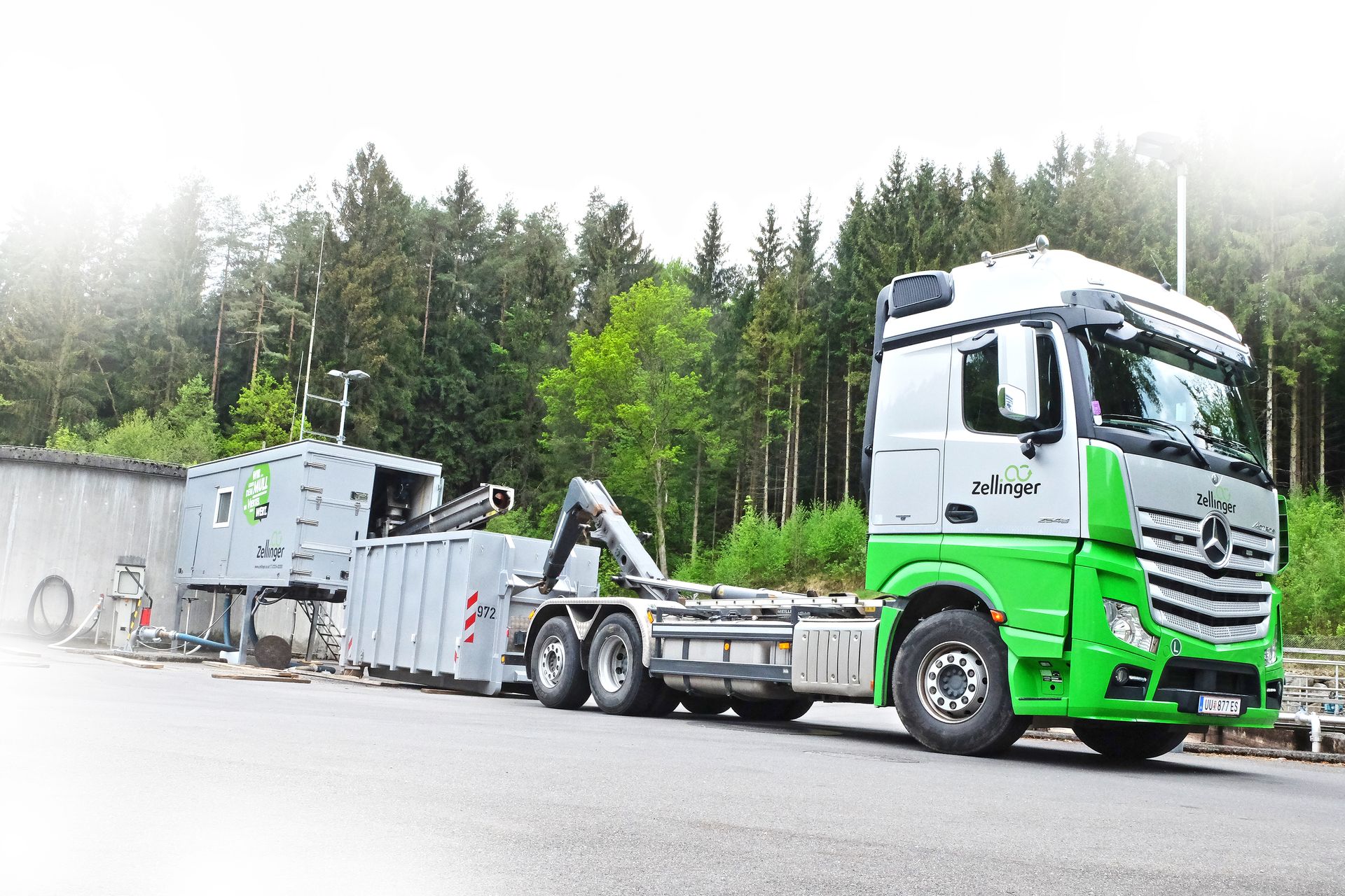 Green and silver Mercedes semi-truck pulling a container, parked on a road with forest background.