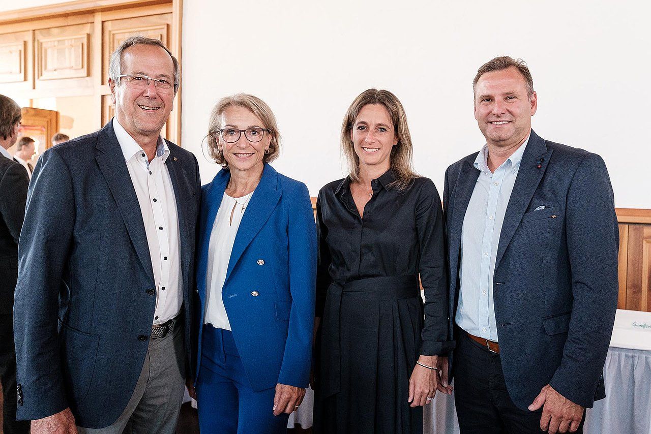 Four people, two men and two women, pose smiling indoors.