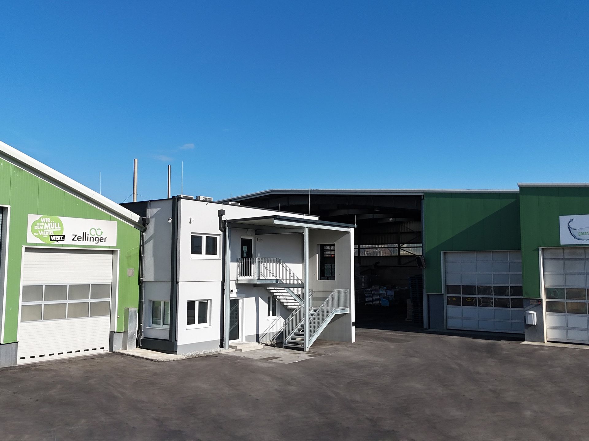 A multi-building complex, gray and green, with offices and garages under a clear blue sky.
