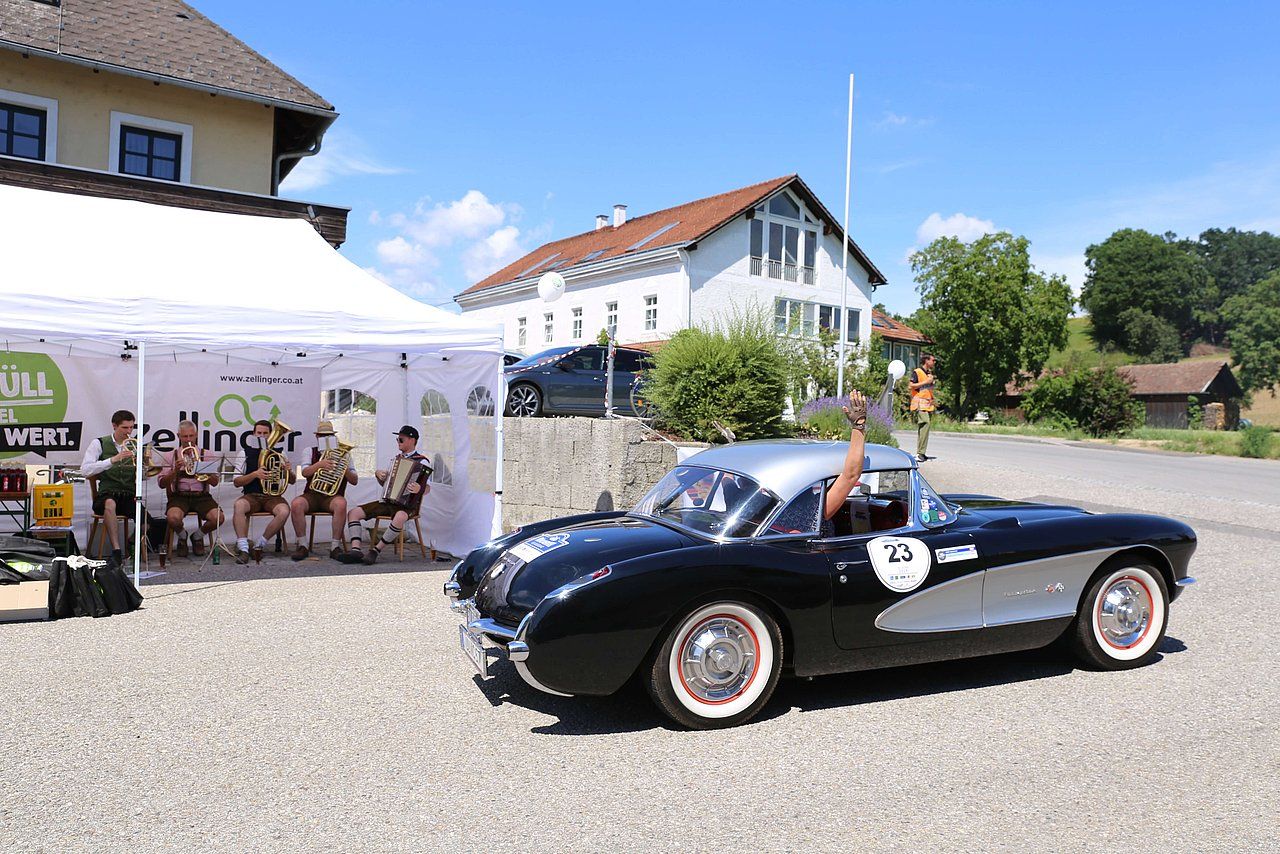Black classic car with silver top, beside a tent and a group of people, outside.