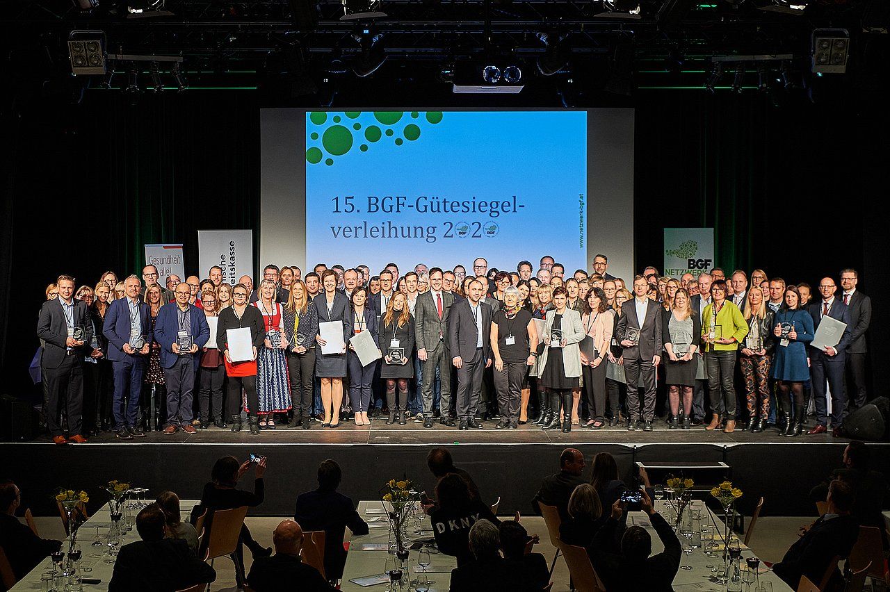 Group of people on a stage holding awards and certificates after an event. A banner is in the background.