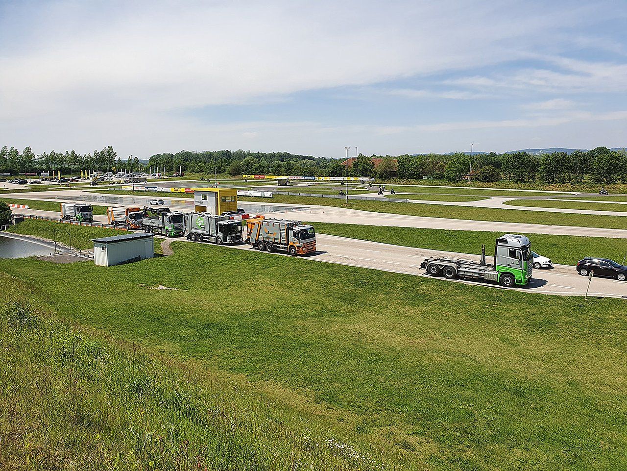 Trucks and construction vehicles parked on grass and dirt, in an open area, under a blue sky.