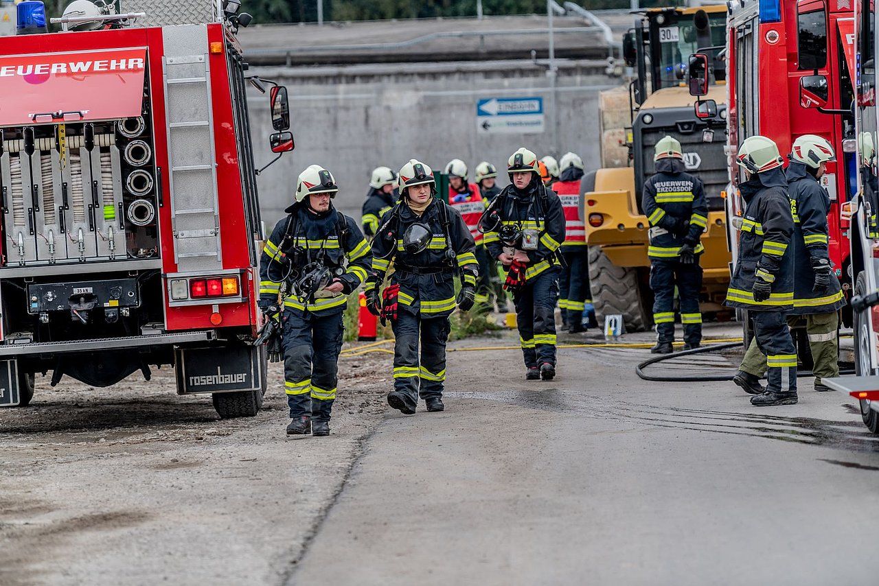 Firefighters in gear walking near fire trucks and heavy machinery.