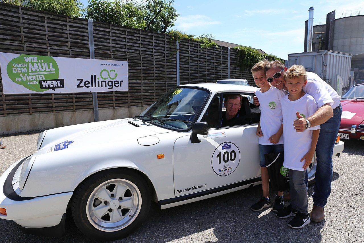 White vintage Porsche with a driver and three boys posing near it.