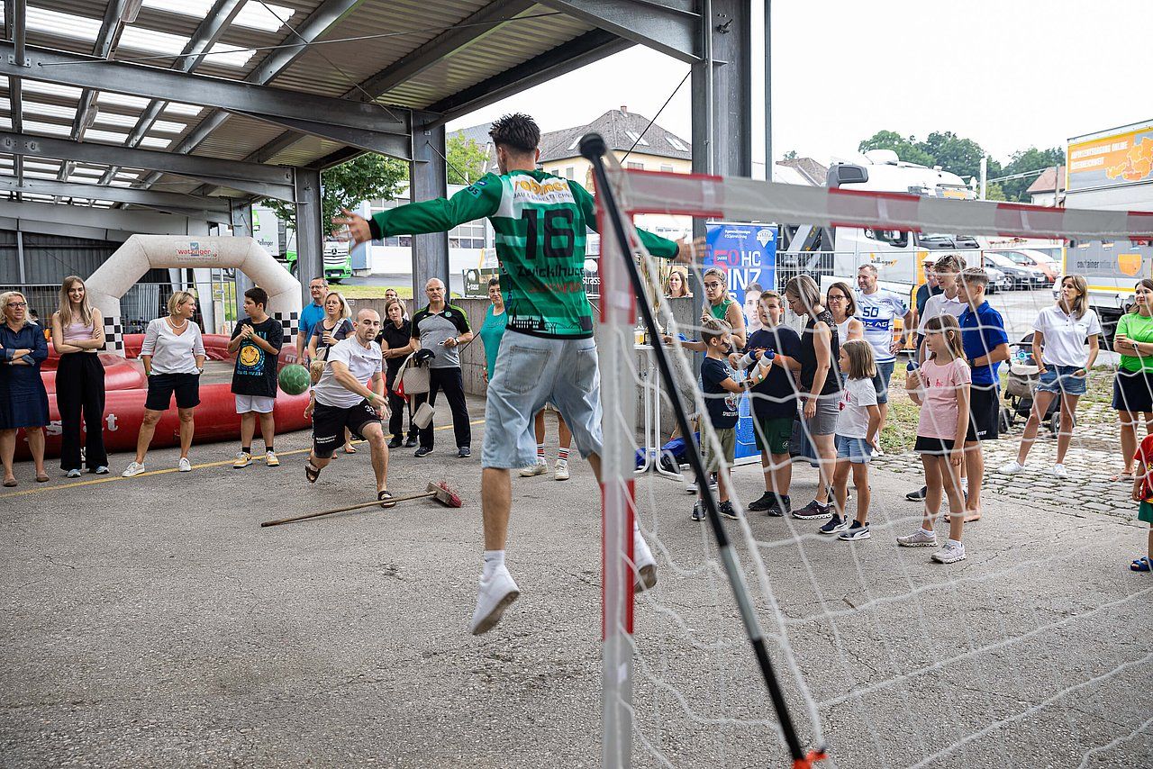 People playing net-based sport, man jumping to hit ball. Crowd watches in covered outdoor area.