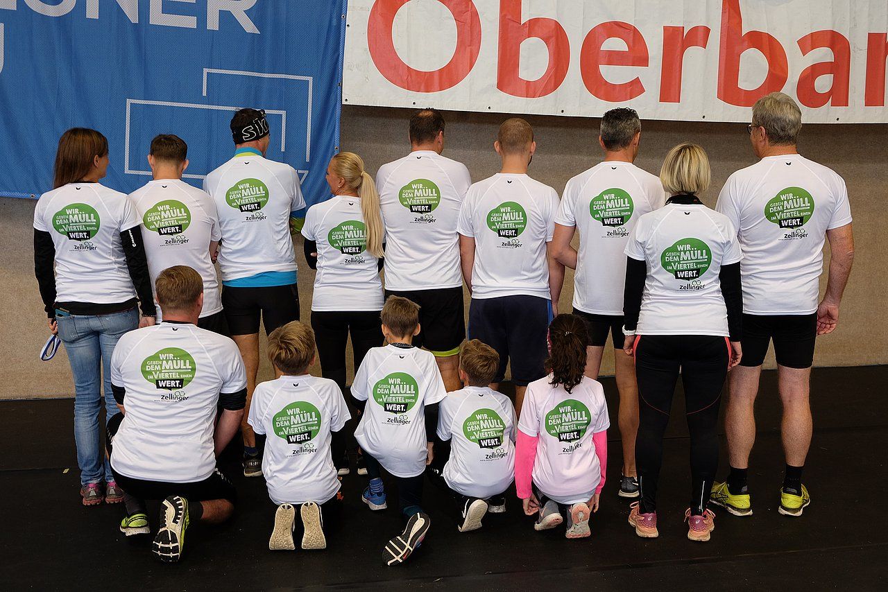 Group of people in white shirts with a green design pose; indoors.