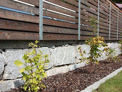 Wooden fence with metal posts over a stone wall, with small plants and mulch along the base.