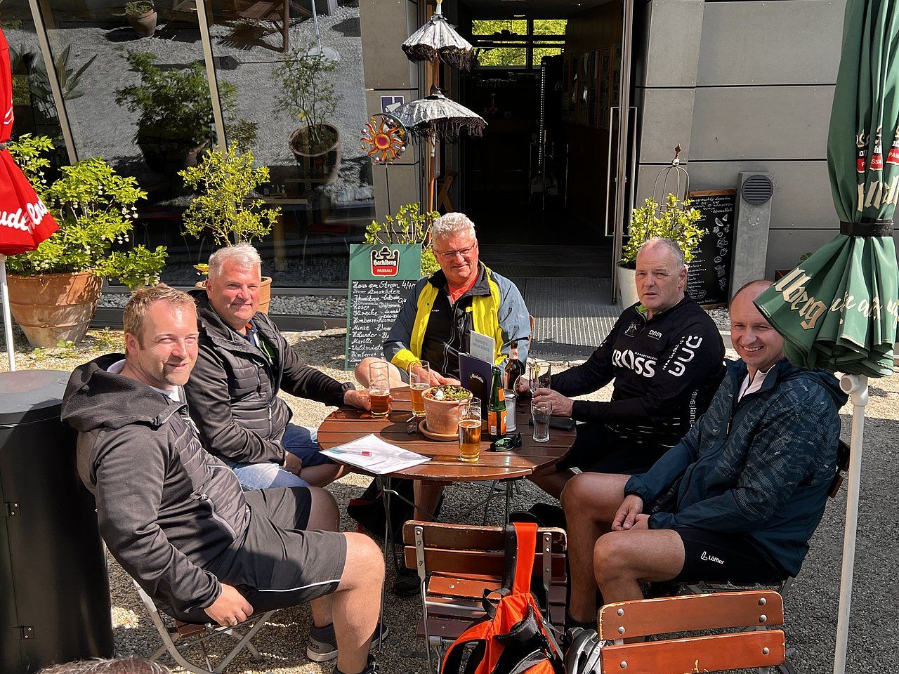 Five men sit at a table outside a cafe, drinking beer and chatting in the sunshine.