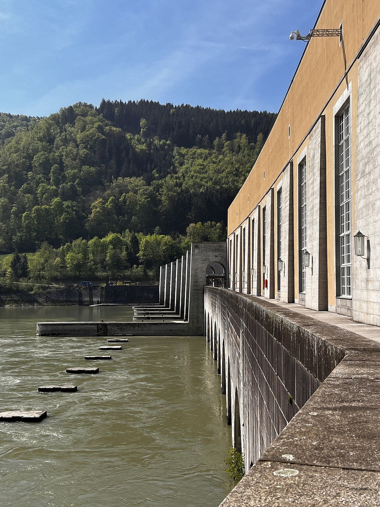 Dam with water flowing through and forested hillside in background.