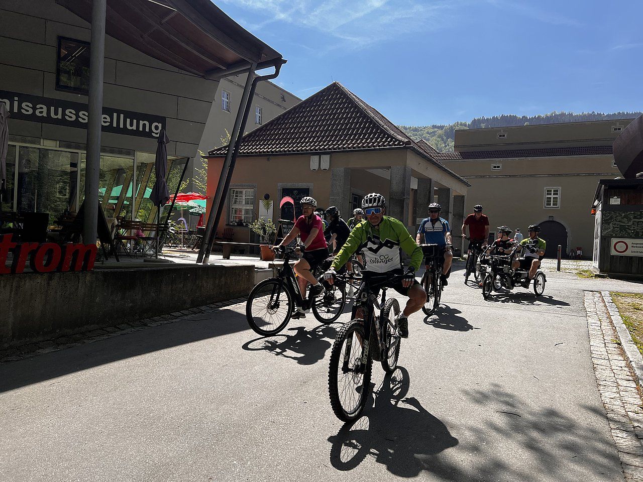 Group of cyclists riding bikes on a paved road next to buildings.