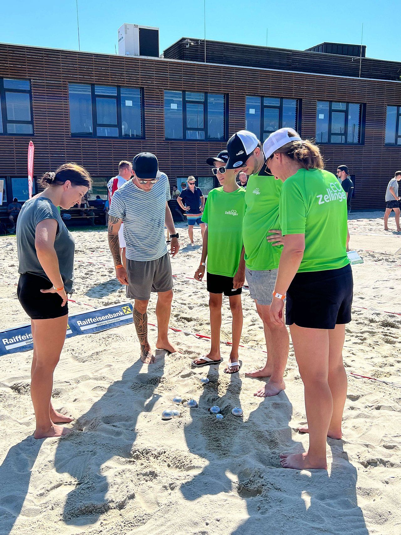 Group of people playing a game on the beach, looking at small objects in the sand.