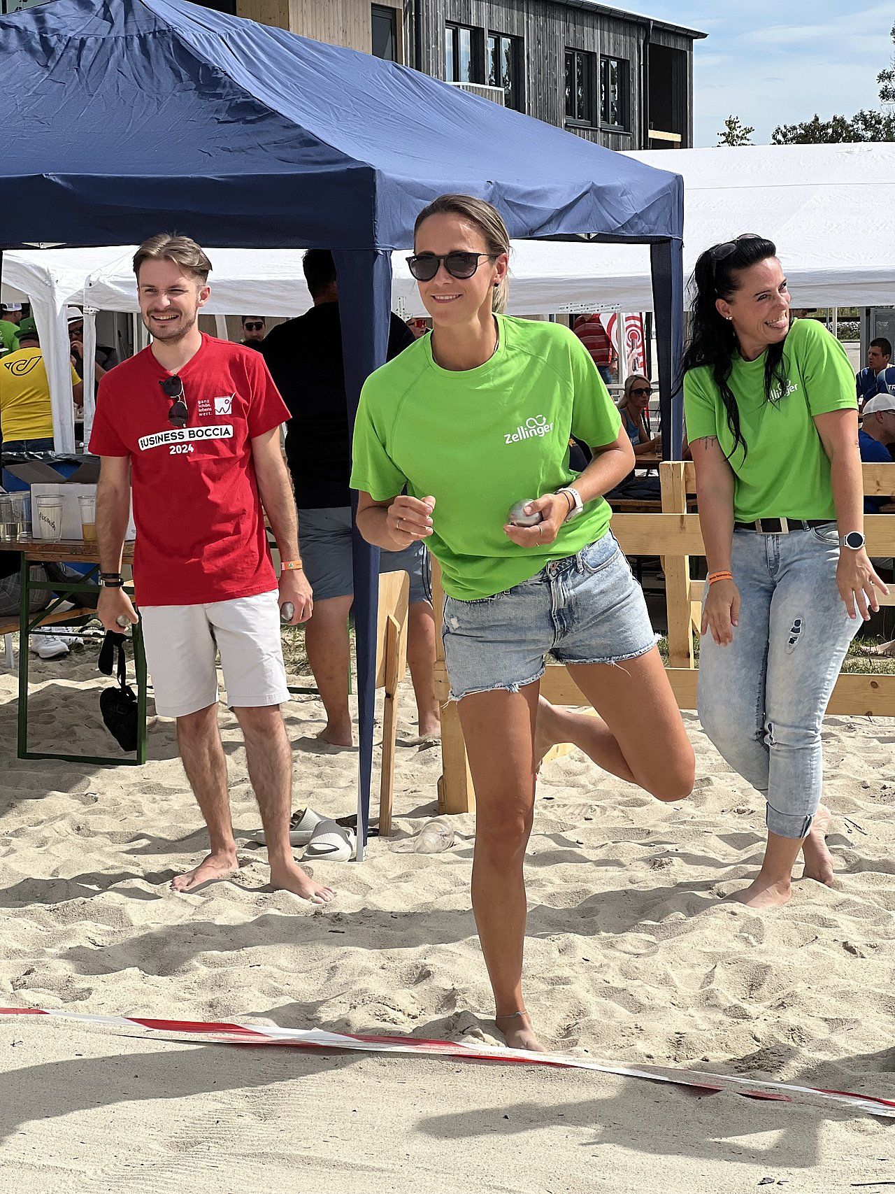 People on sandy beach, woman in green shirt balances, others watch.