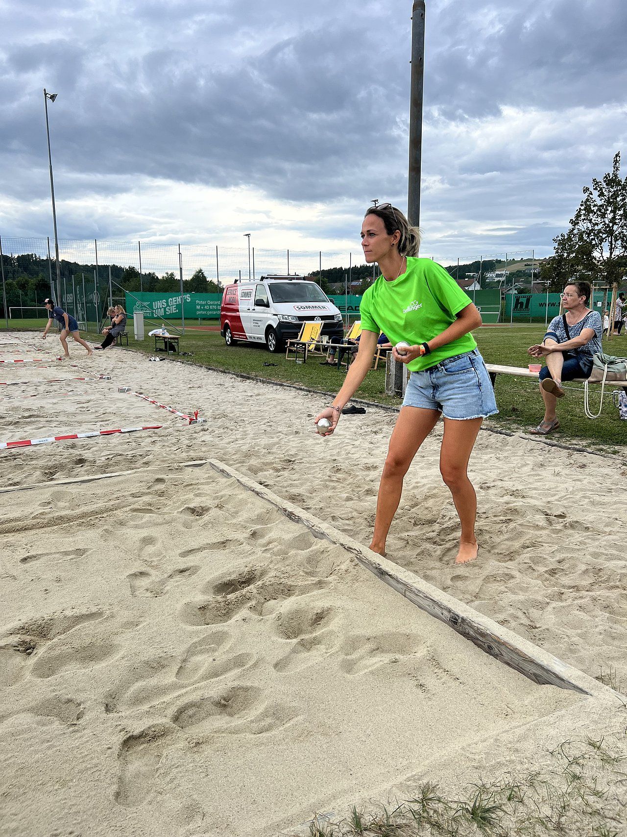 Woman in green shirt throws a ball on a sand court.