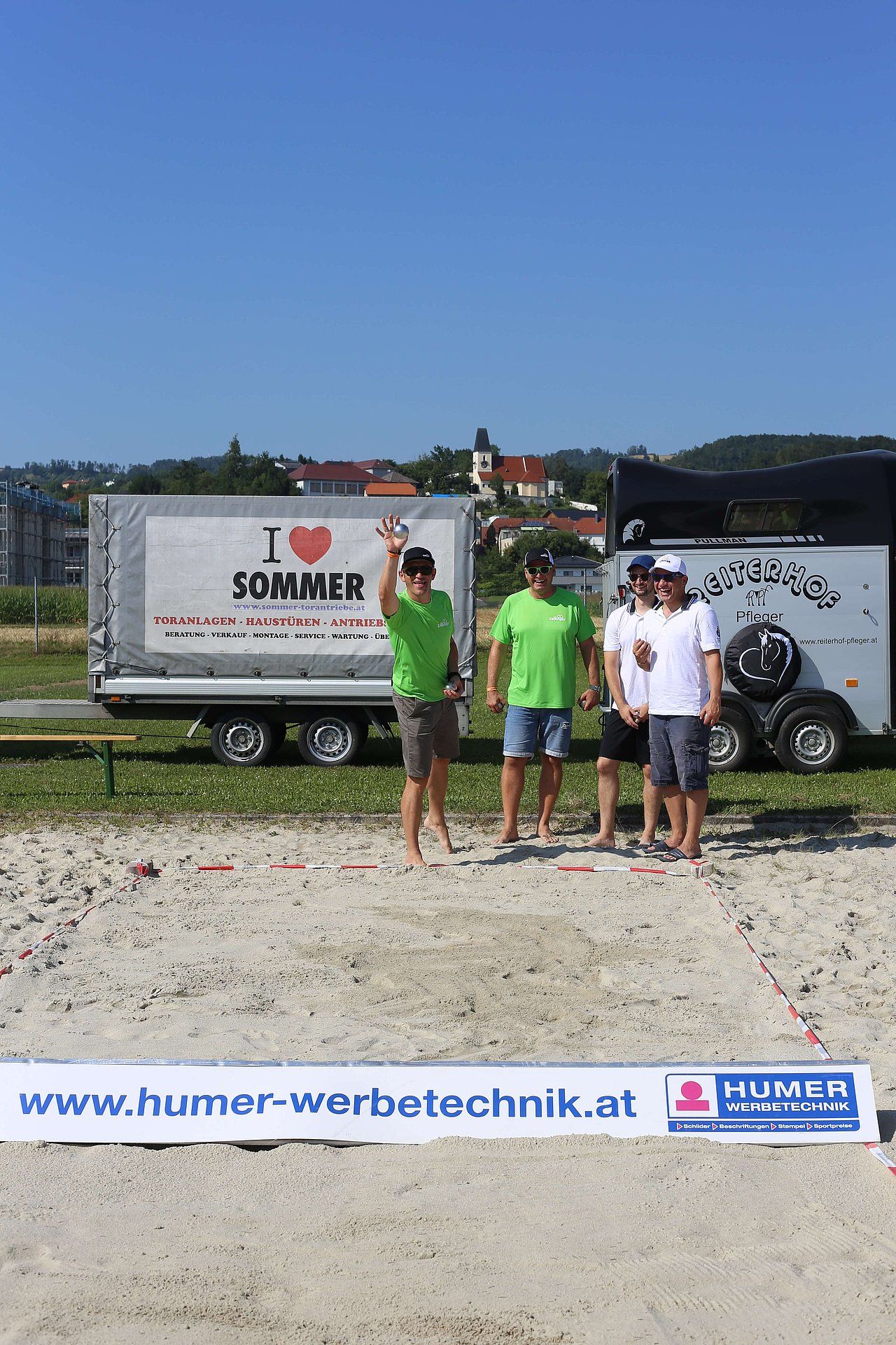 Men playing a game outdoors on a gravel court, next to trailers. 