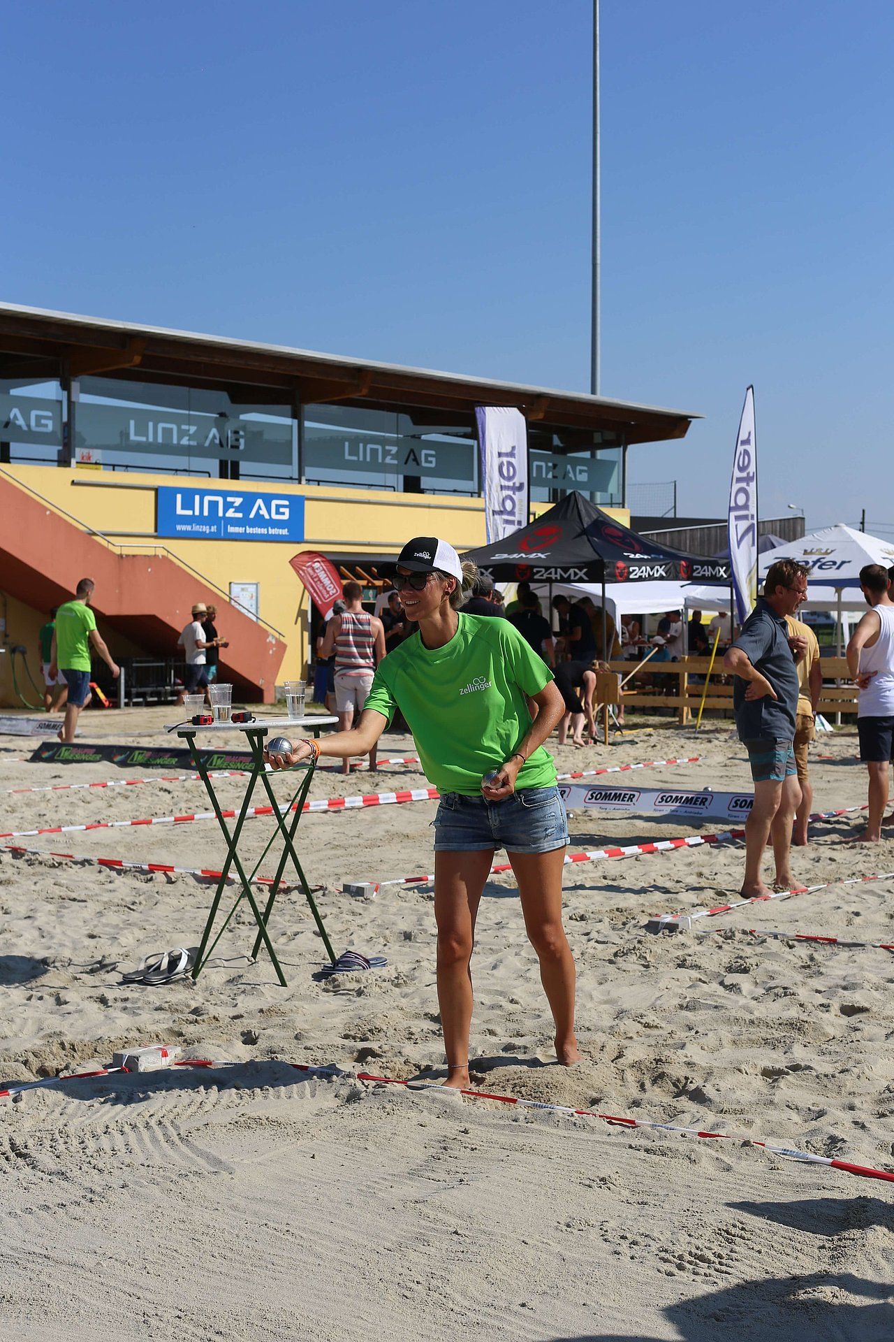 Woman in green shirt throws something at a target on a sandy beach, sunny day.
