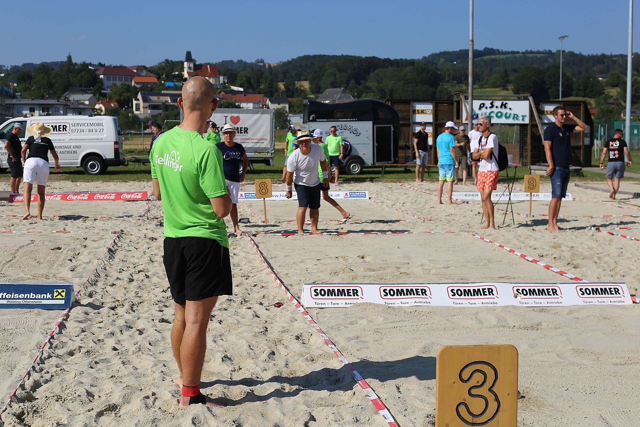 Beach volleyball players on sandy court, spectators, sunny day.