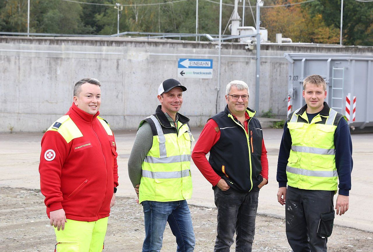 Four workers in safety vests stand in front of a concrete structure, smiling.