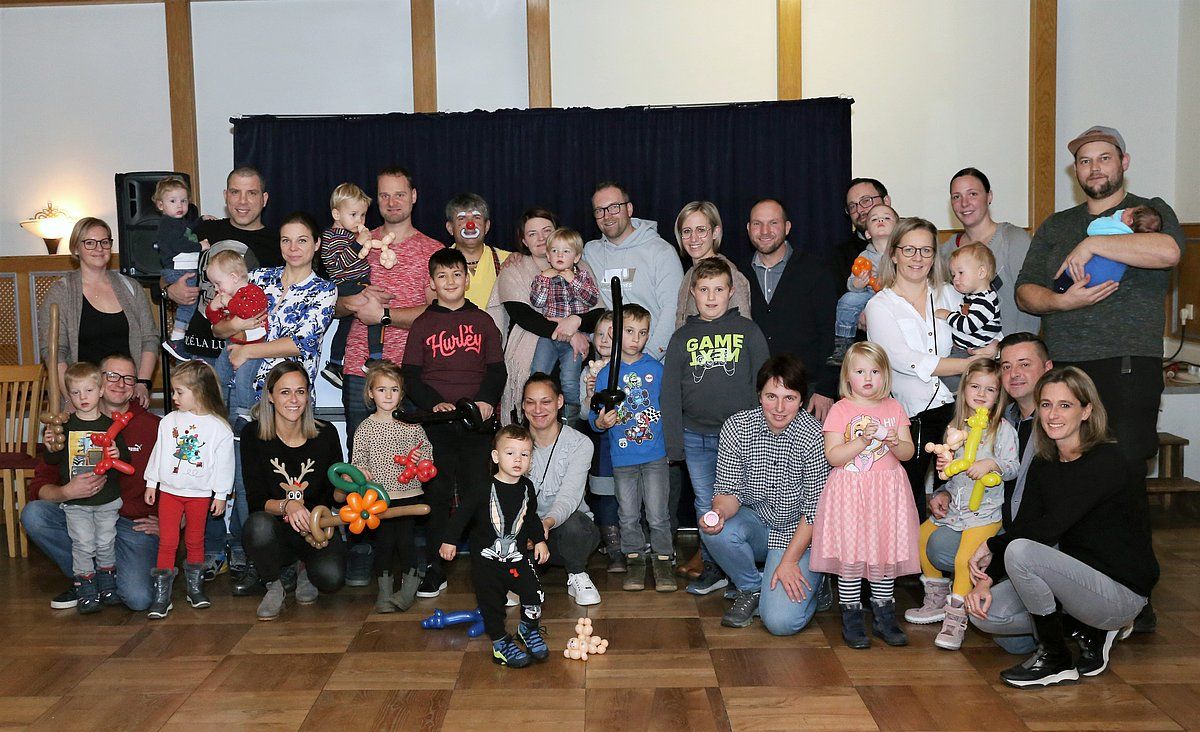 Large group of people, many children, posing for a photo indoors.  Smiling faces, various ages, near a wooden wall.
