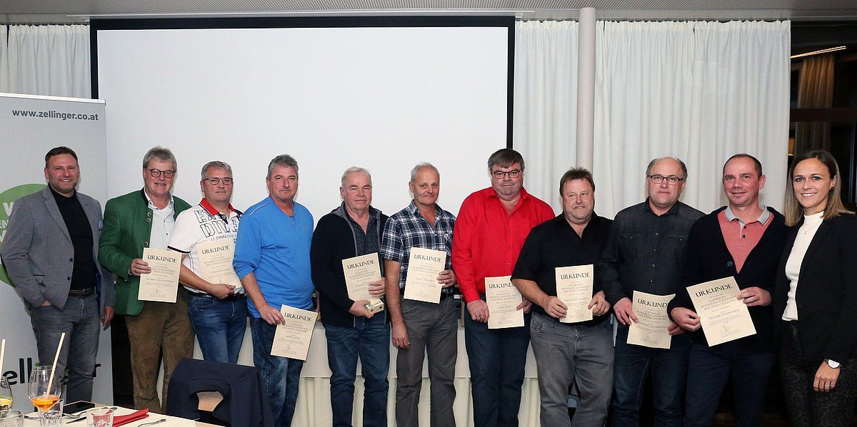 A group of men and a woman holding certificates, standing in front of a white screen, indoors.