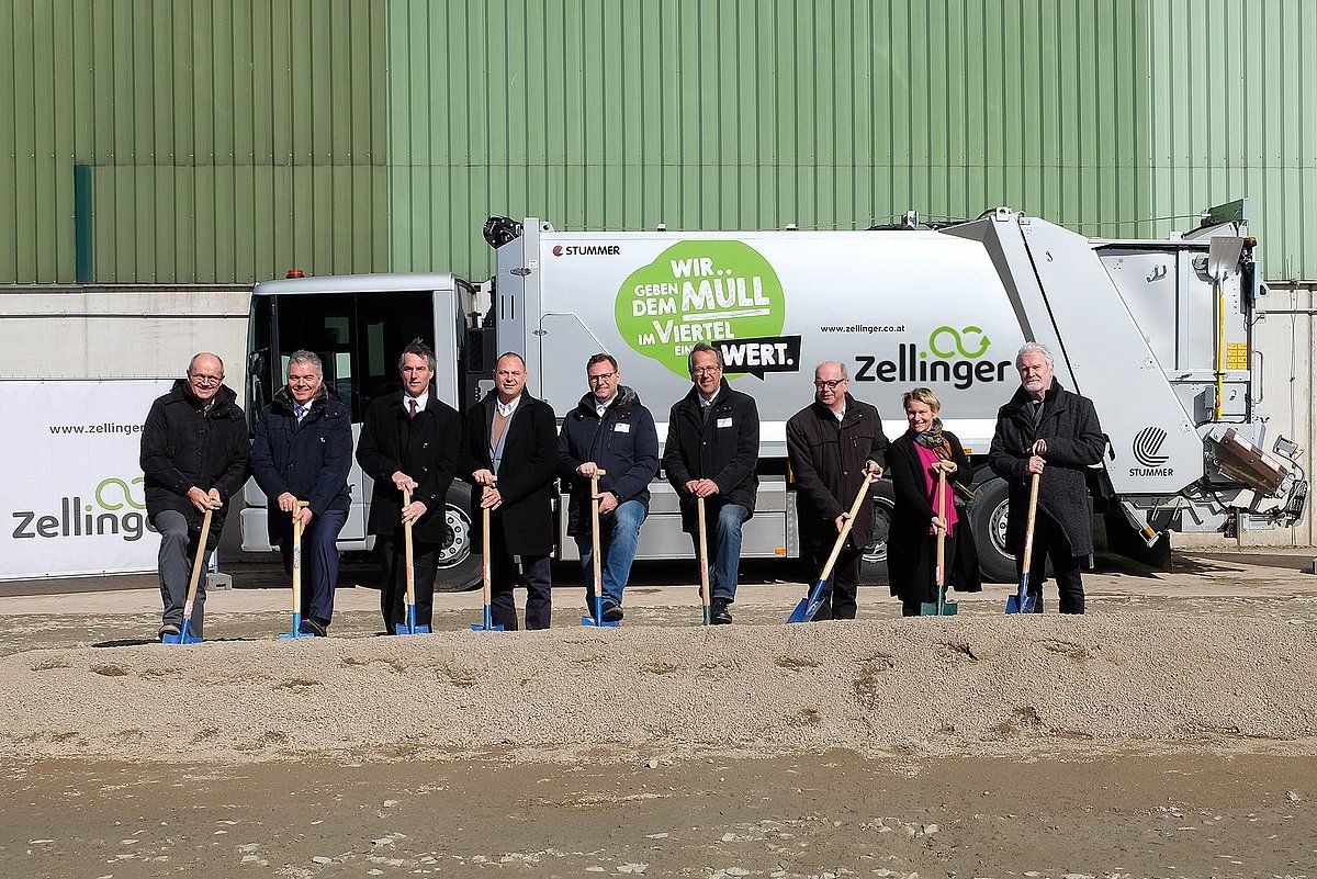 Group of people holding shovels in front of a waste disposal truck, presumably at a ground-breaking ceremony.
