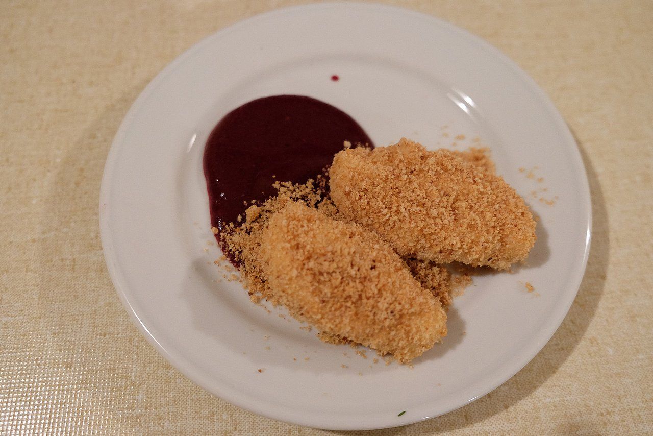 Two golden-brown dumplings in breadcrumbs with dark berry sauce on a white plate.