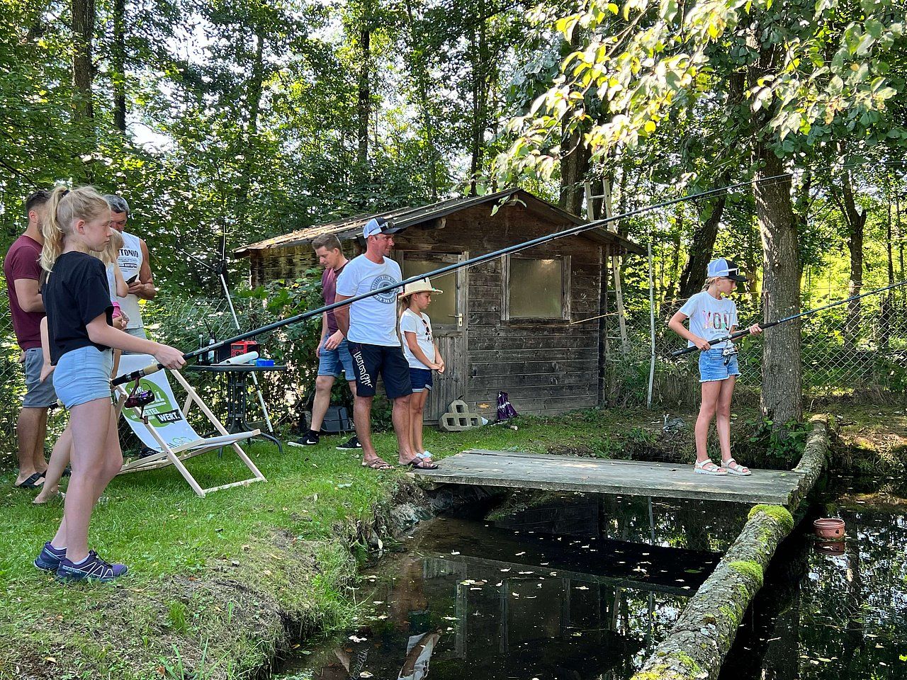 People fishing at a pond with a small wooden cabin in the background.