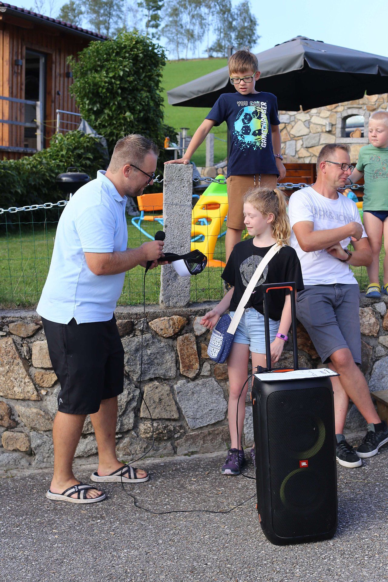 Man with microphone, recording a girl; other people nearby. Outdoor setting.