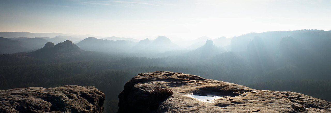 Rocky mountaintop overlooking a hazy valley with sunlight.