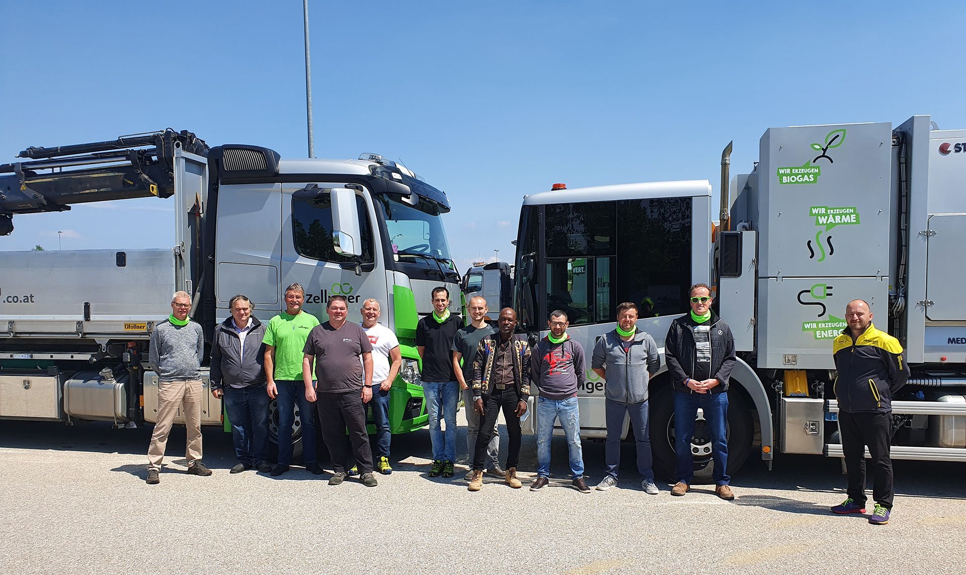 Group of men standing in front of two large trucks under a clear blue sky.