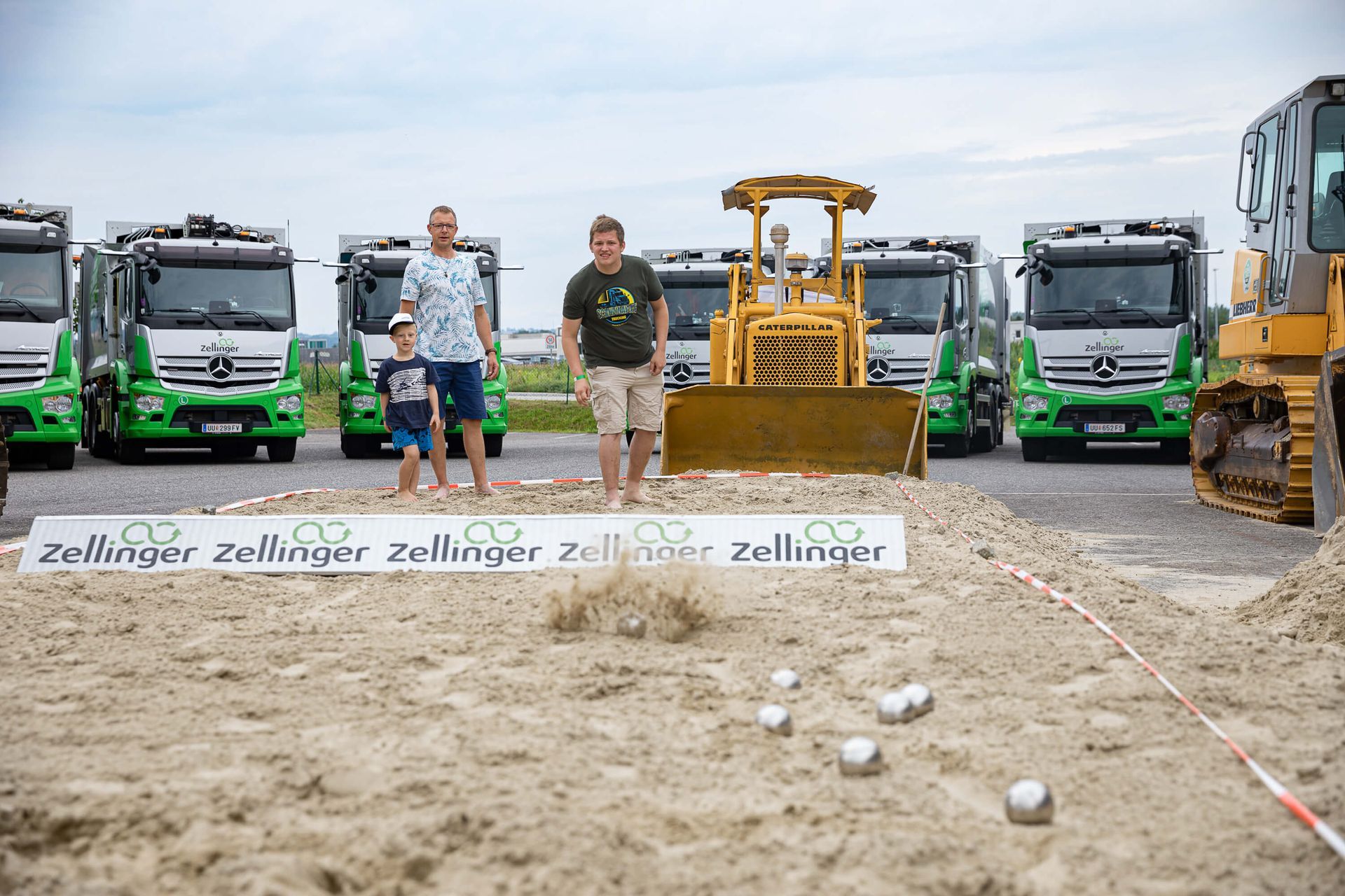 People playing pétanque on sand with construction vehicles in the background.