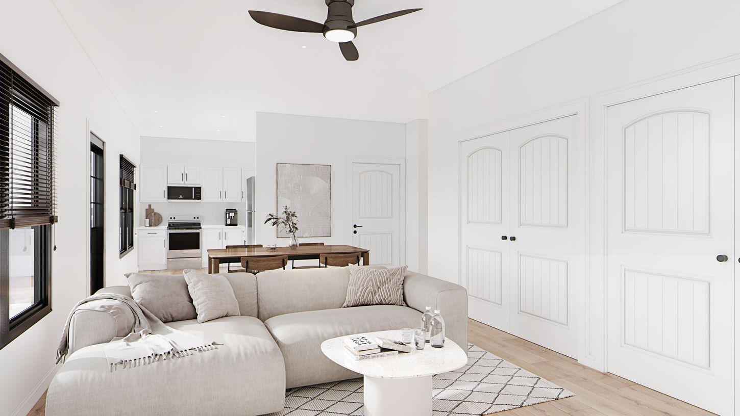 Bright white living room with sectional sofa, round coffee table, wall paneling, and ceiling fan.