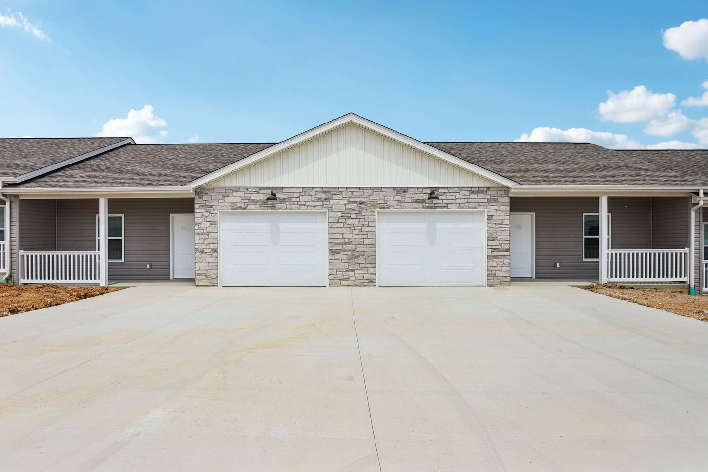 Front view of a duplex with two white garage doors and a wide concrete driveway under a blue sky