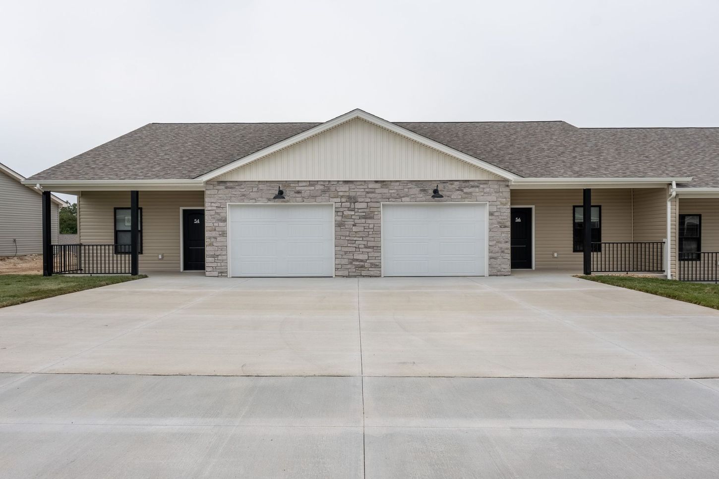 Two-story duplex with a beige brick facade and two white garage doors on a concrete driveway