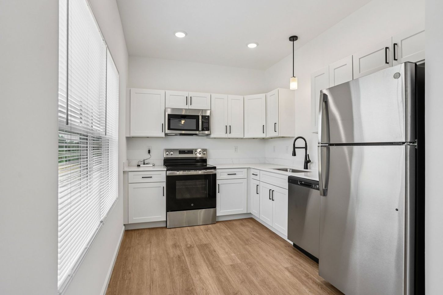 Bright modern kitchen with white cabinets, stainless steel appliances, and wood-look flooring.