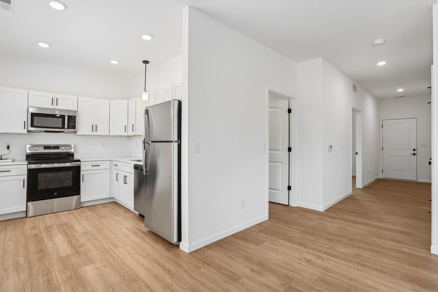 Bright white kitchen and hallway with stainless steel appliances and light wood floors
