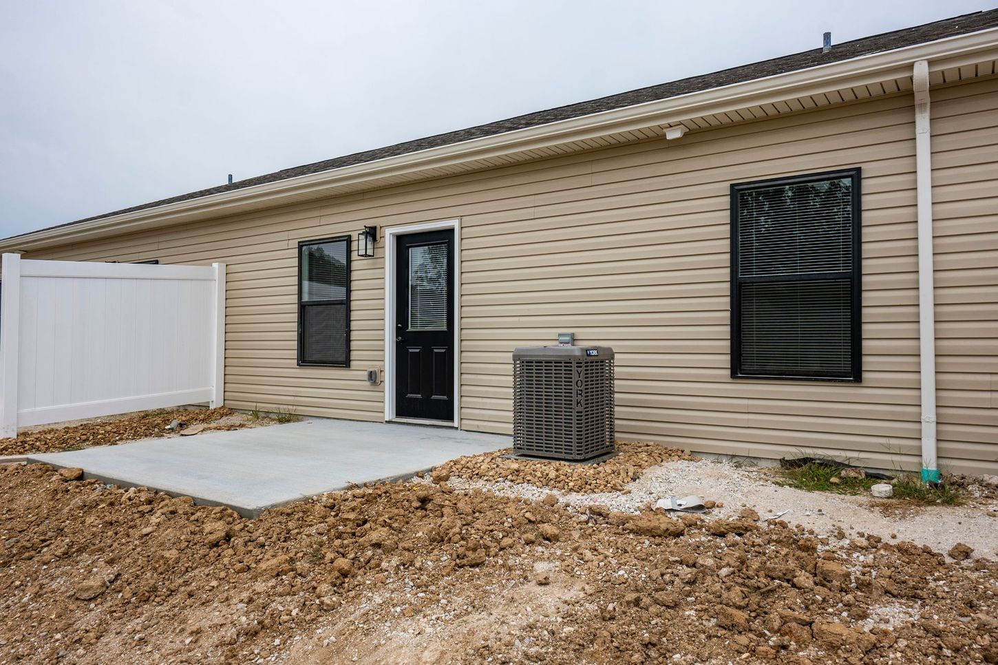 Backyard patio with beige house siding, black doors and windows, and a white privacy fence.