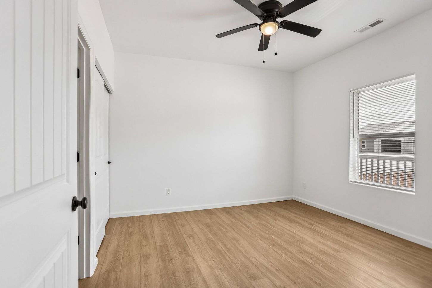 Empty white bedroom with light wood floors, a ceiling fan, and a window