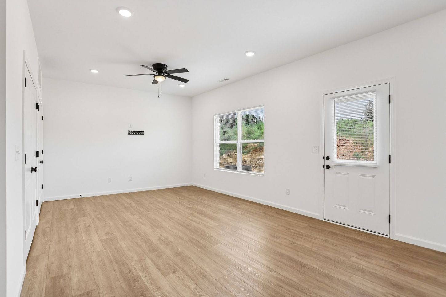 Empty white room with wood flooring, recessed lights, ceiling fan, and two windows beside a door