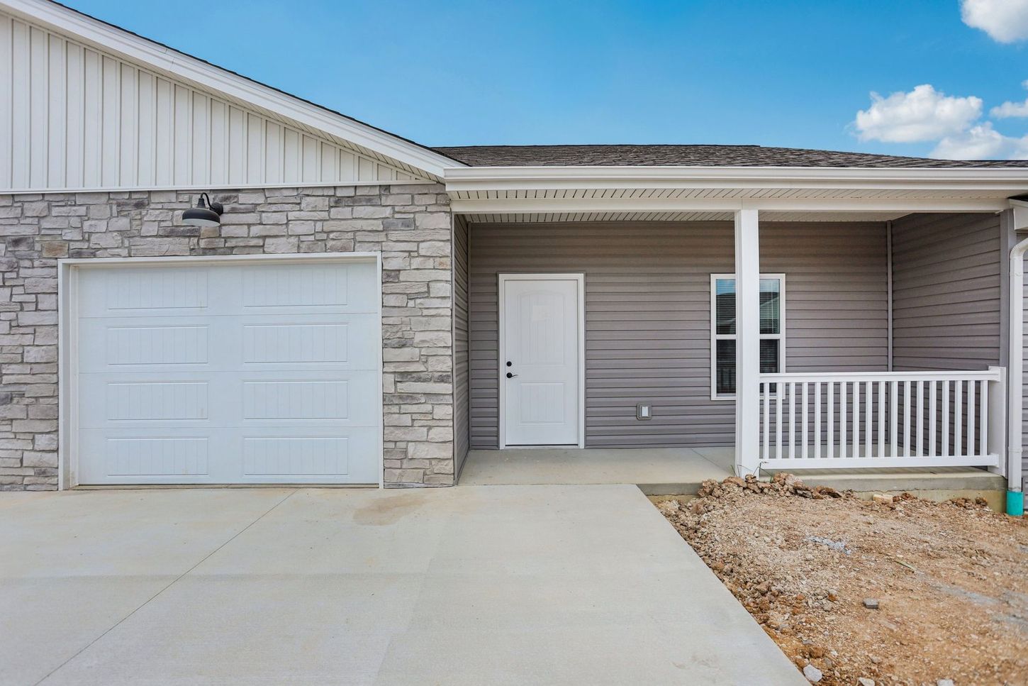 Modern single-story house exterior with white garage door, stone siding, and covered porch