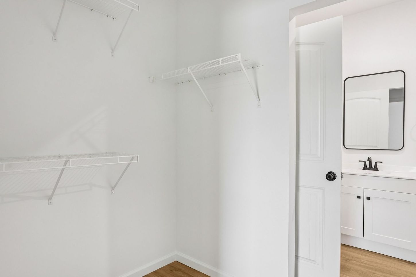 Empty white walk-in closet with wire shelves and a doorway to a bathroom with sink and mirror