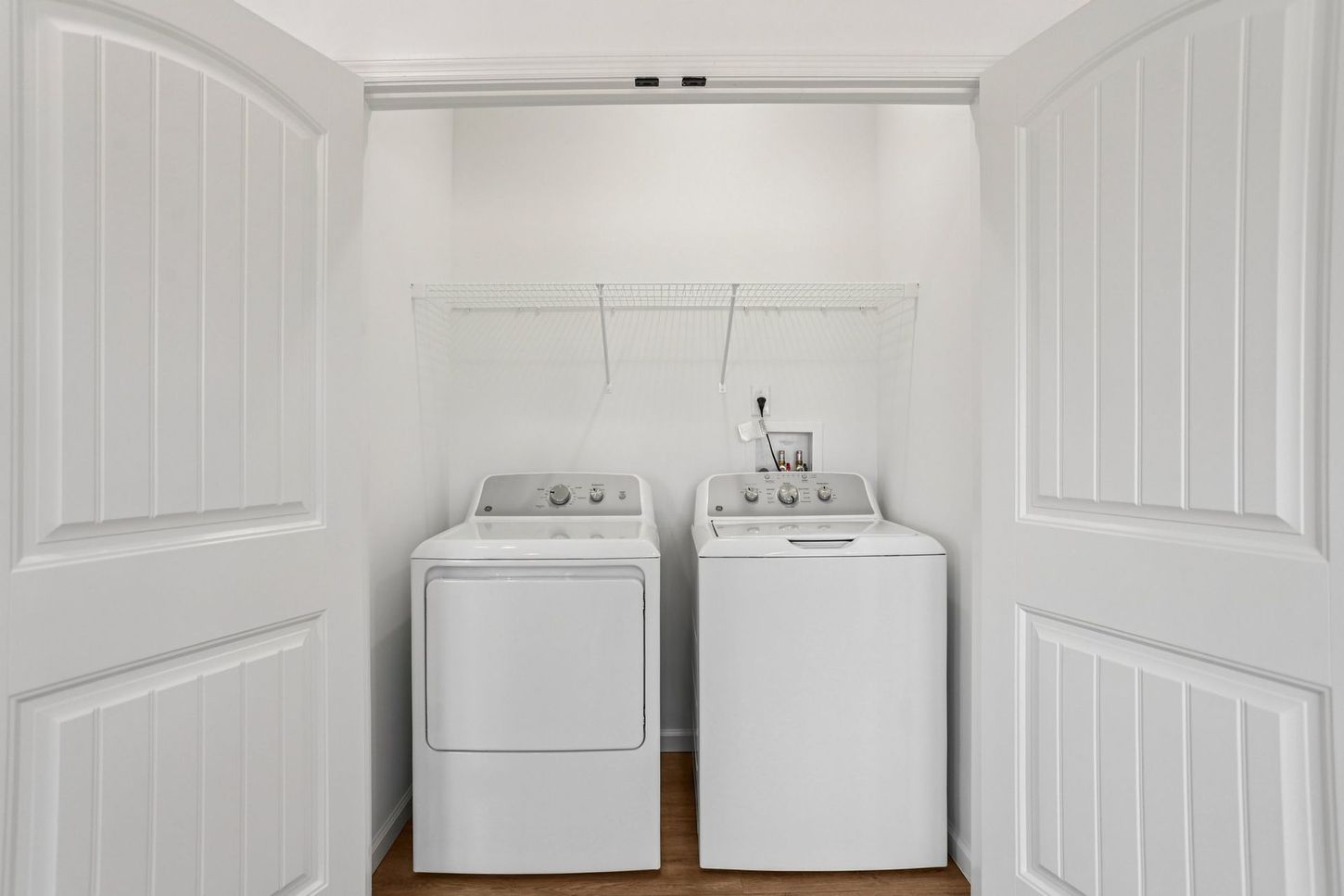 Laundry room with a white washer and dryer behind open white double doors.