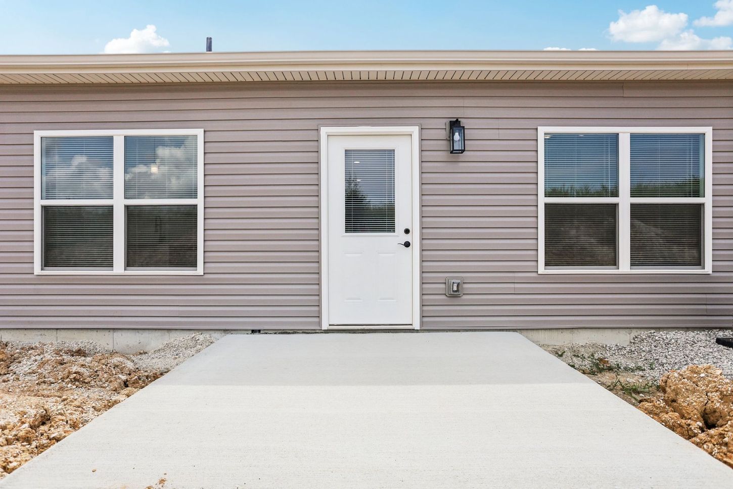 Front view of a beige manufactured home with white door, windows, and a concrete walkway