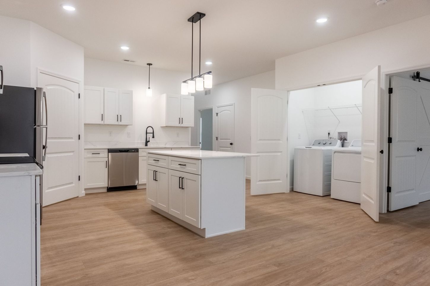 Bright modern white kitchen with island, pendant lights, stainless appliances, and wood floors
