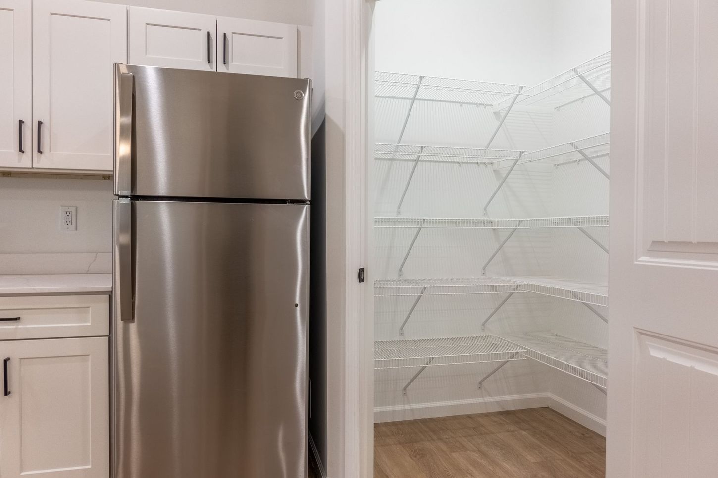White kitchen with stainless steel refrigerator beside an open pantry with wire shelving